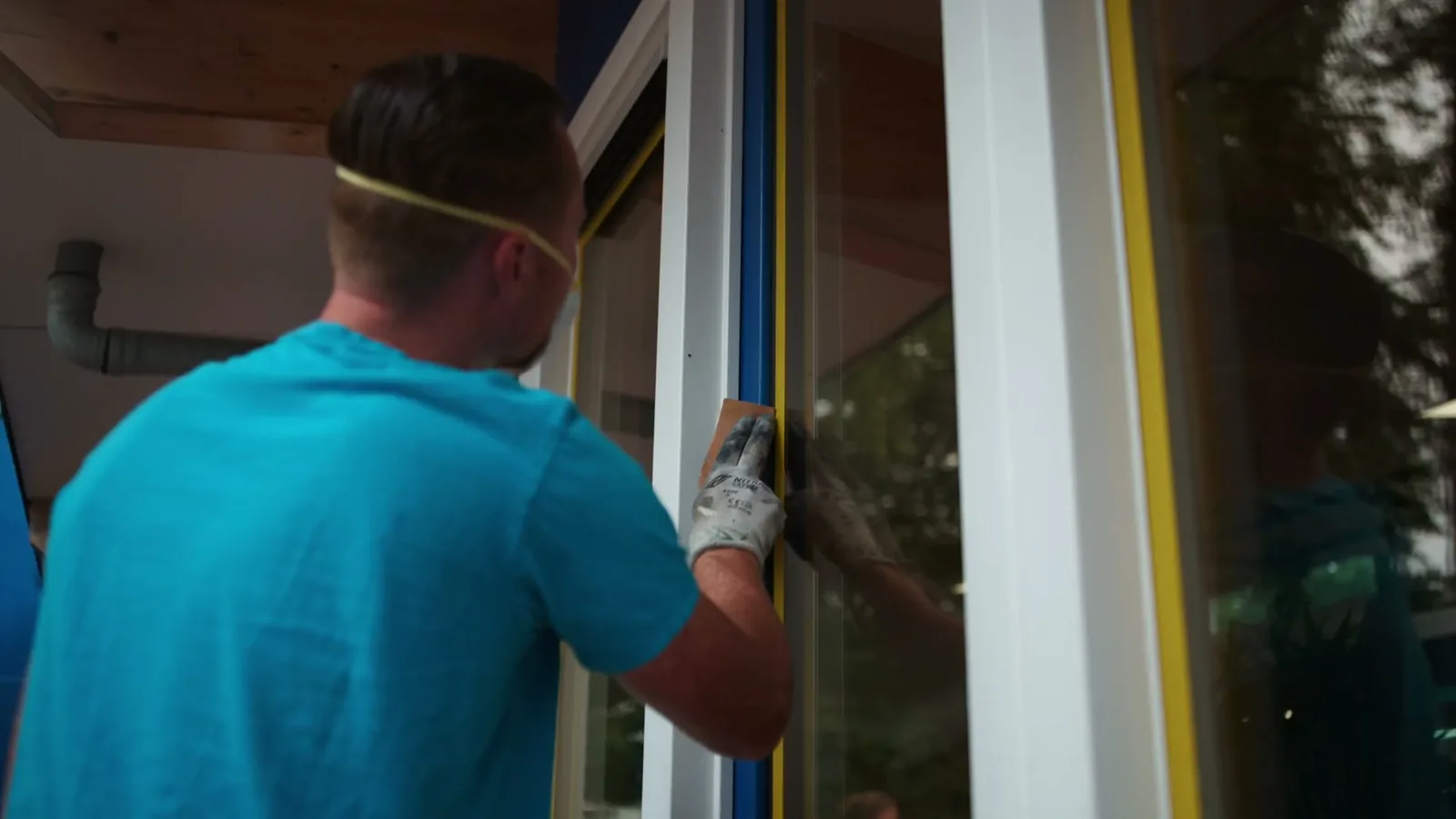 Schilder van Van Foeken werkt met stofmasker aan een raam